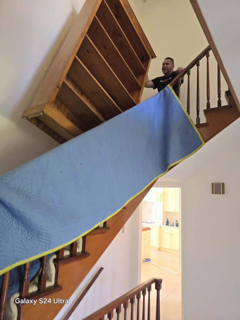 Large timber cabinet being moved down narrow stairs
