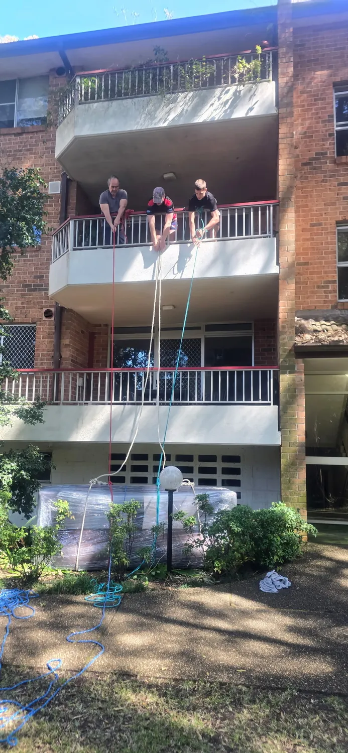 Careful Movers crew lowering a wrapped lounge from a second floor balcony in Hornsby